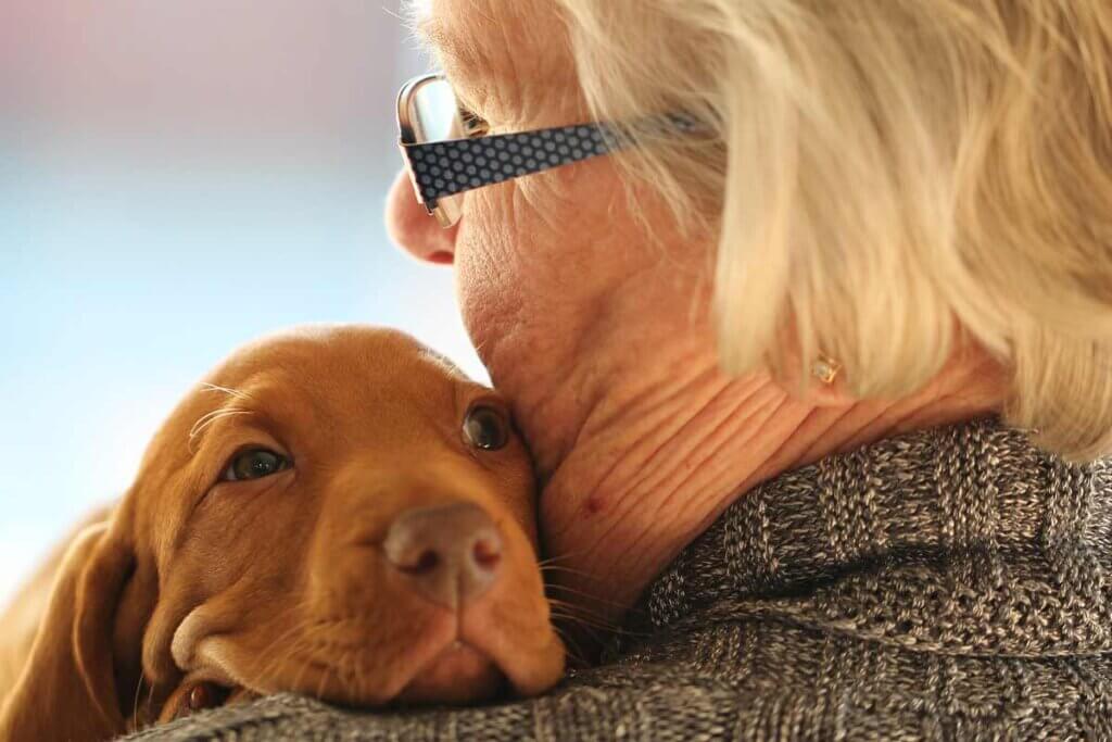 Alte Frau traegt Hund im Arm