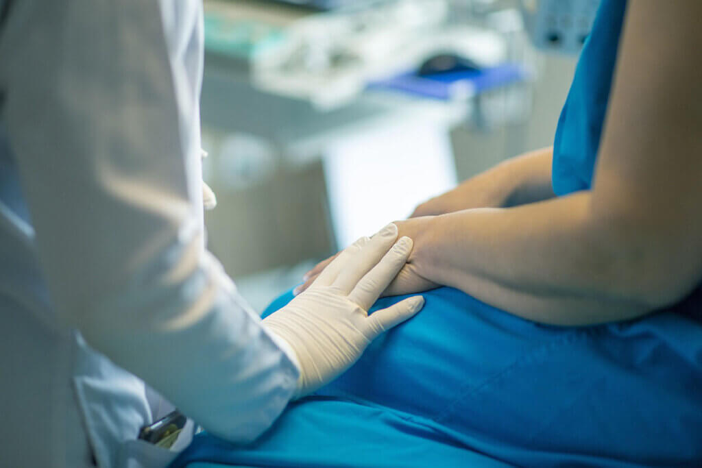 Eine Person in Kittel und Handschuhen spricht mit einer Person in einem blauen Kittel im Krankenhaus.