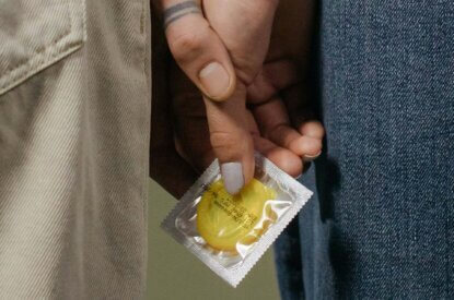 Zwei Personen stehen nebeneinander und halten ein gelbes Kondom fest.