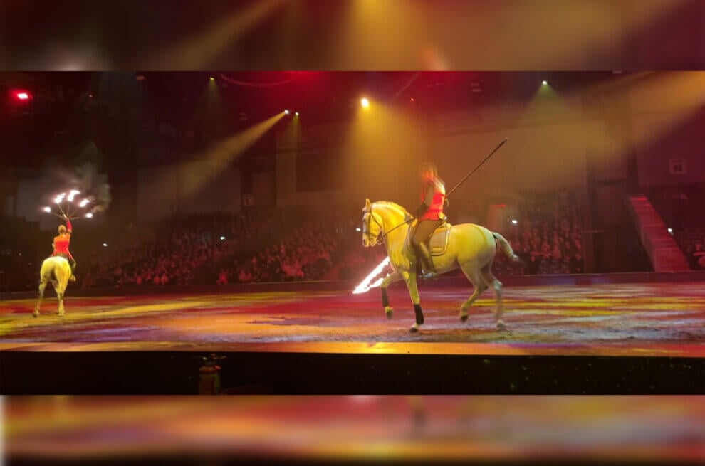 Pferde in der Manege: Die Reiter haben angezündete Objekte und schwingen diese in während dem Reiter in der Nähe der Pferde.