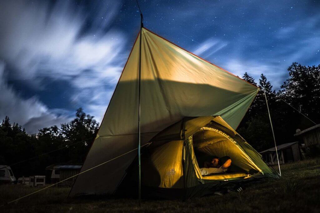Eine Person liegt in einem gelben Zelt unter dem Sternenhimmel.