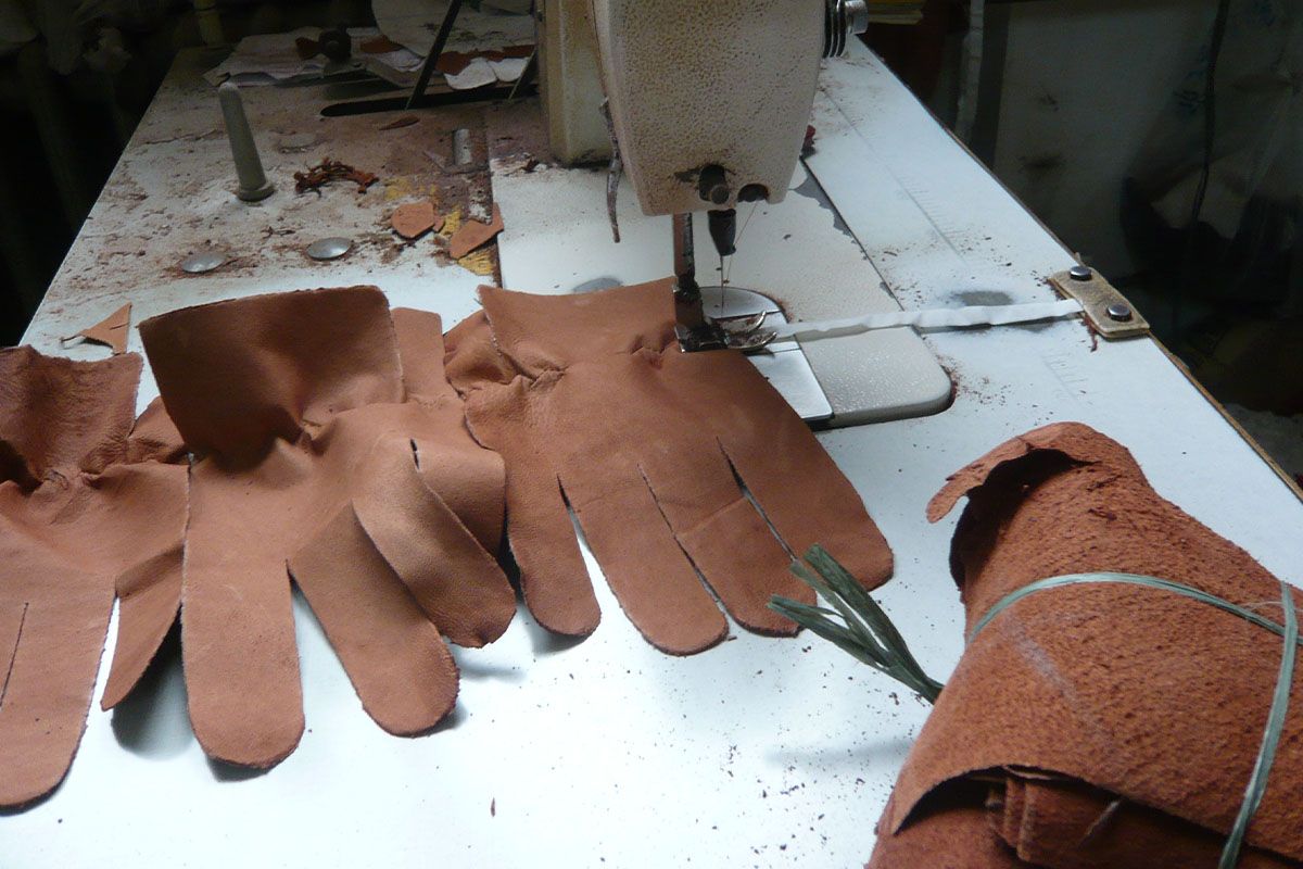 Ein Muster von Handschuhen aus Hundeleder liegt neben einer Naehmaschine.