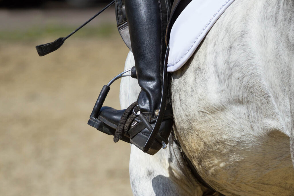 Person sitzt auf Pferd mit Peitsche und Sporen an den Schuhen 