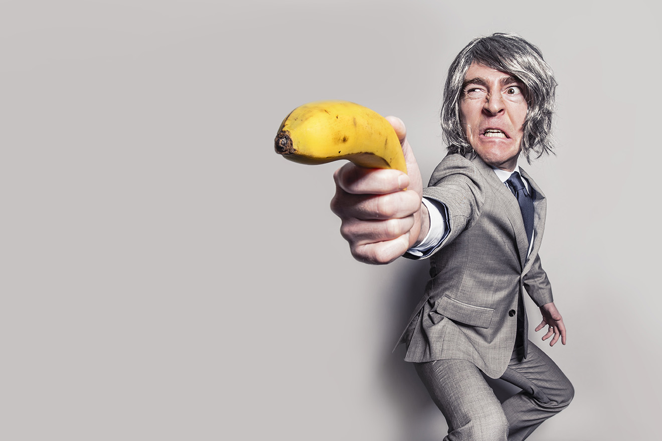 Ein Mann im grauen Anzug, der eine Banane wie eine Pistole hält