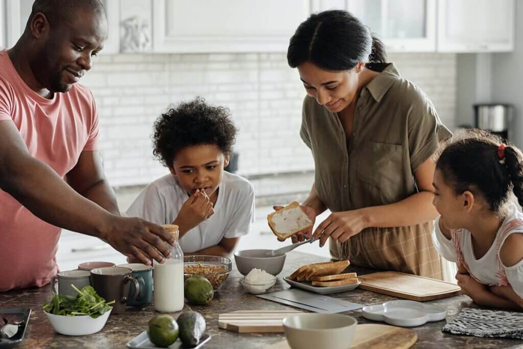Eine Familie steht an einer Kuecheninsel und bereitet ein Fruehstueck zu.