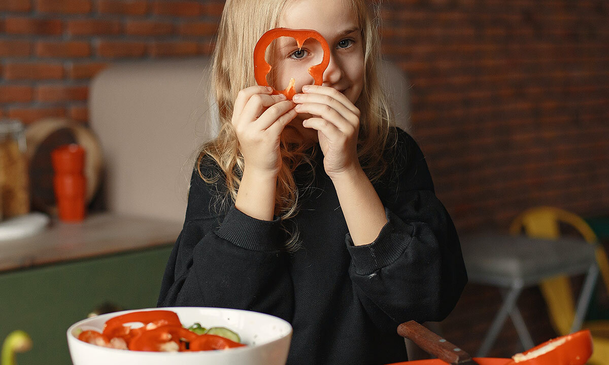 Ein Kind haelt eine Scheibe Paprika vor das Gesicht.