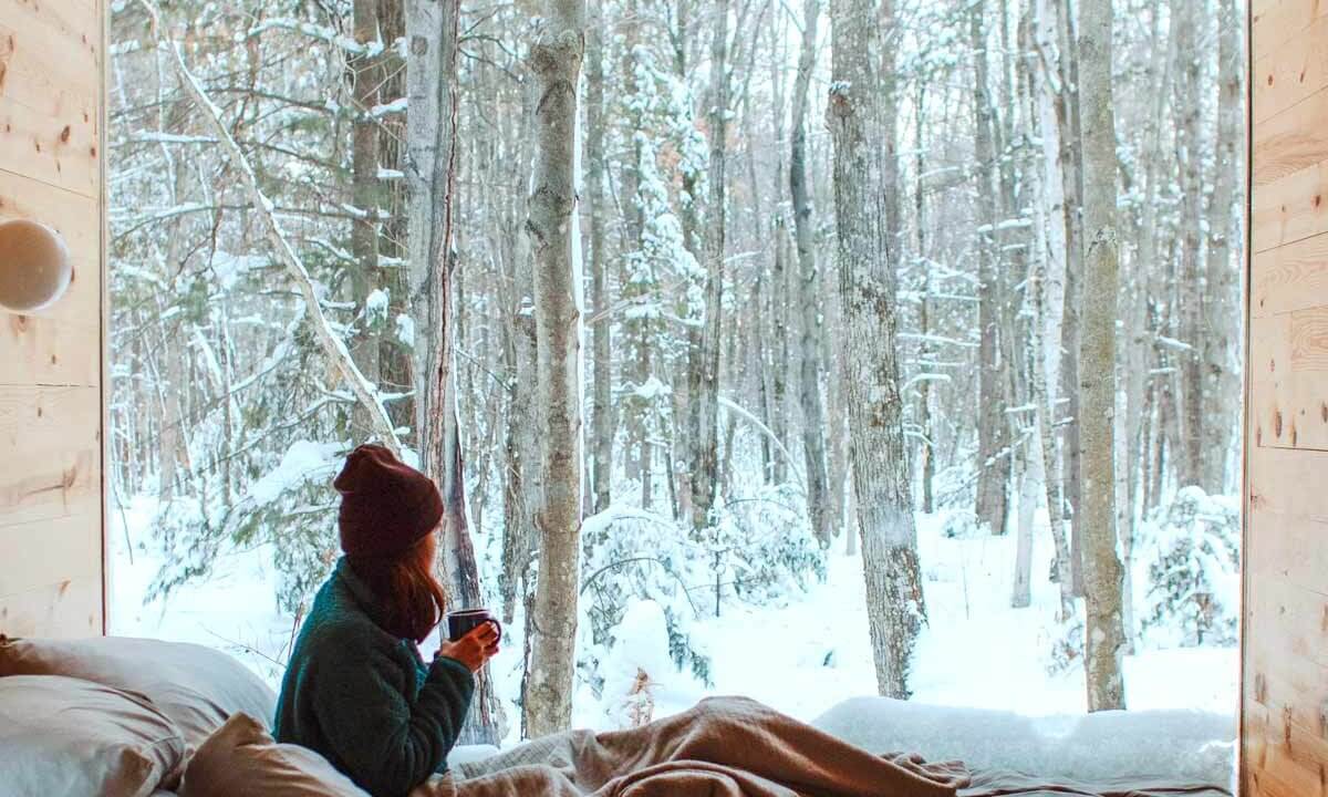 Frau sitzt im Bett vor einem Fenster im Wald
