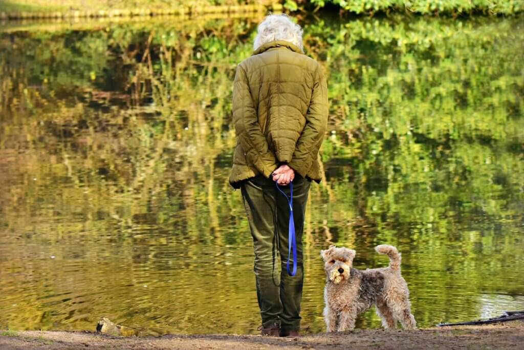 Altere Frau steht mit Hund an einem See