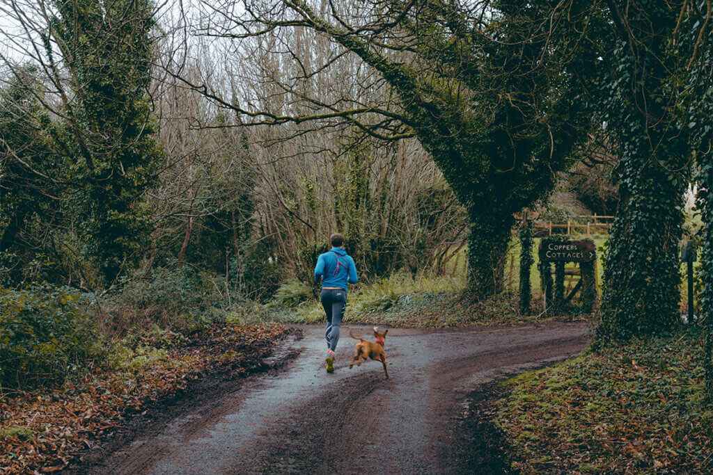 Mensch joggt mit Hund im Wald