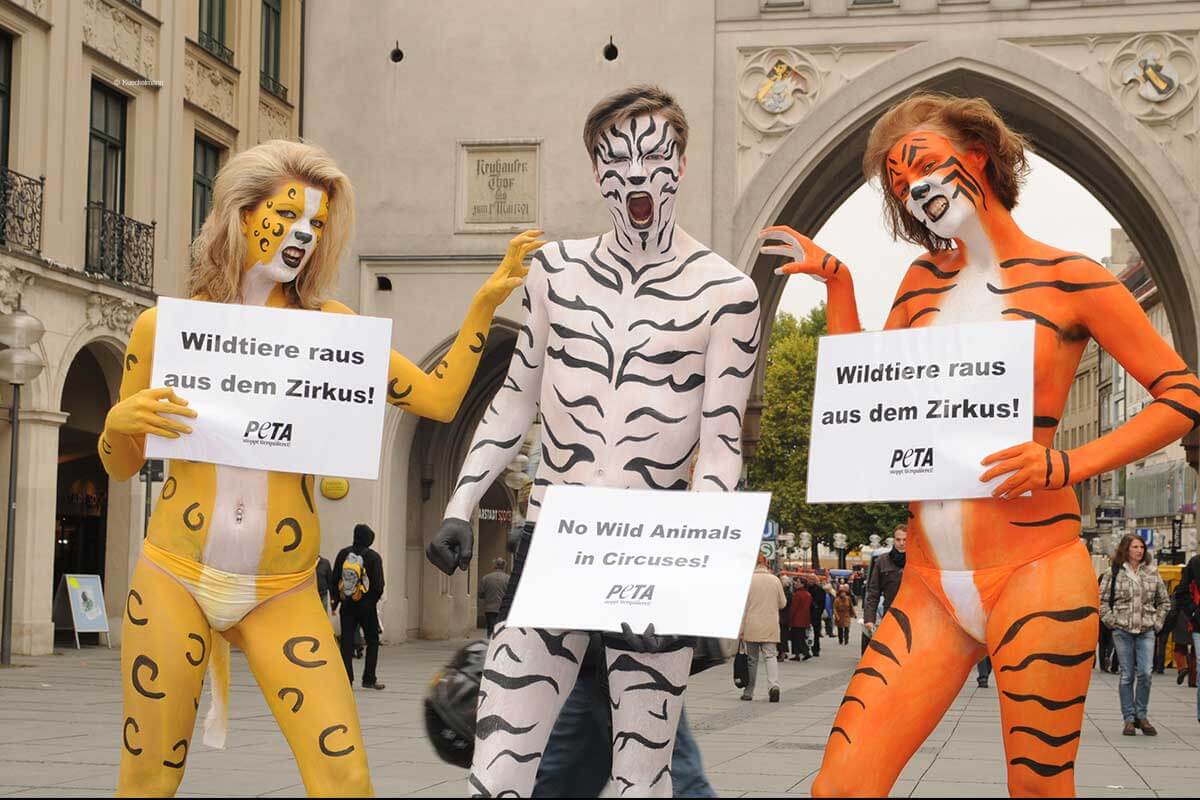 Drei Aktivist:innen demonstrieren in München gegen Wildtiere im Zirkus und sind dazu mit Bodypainting selbst wie Tiere angemalt