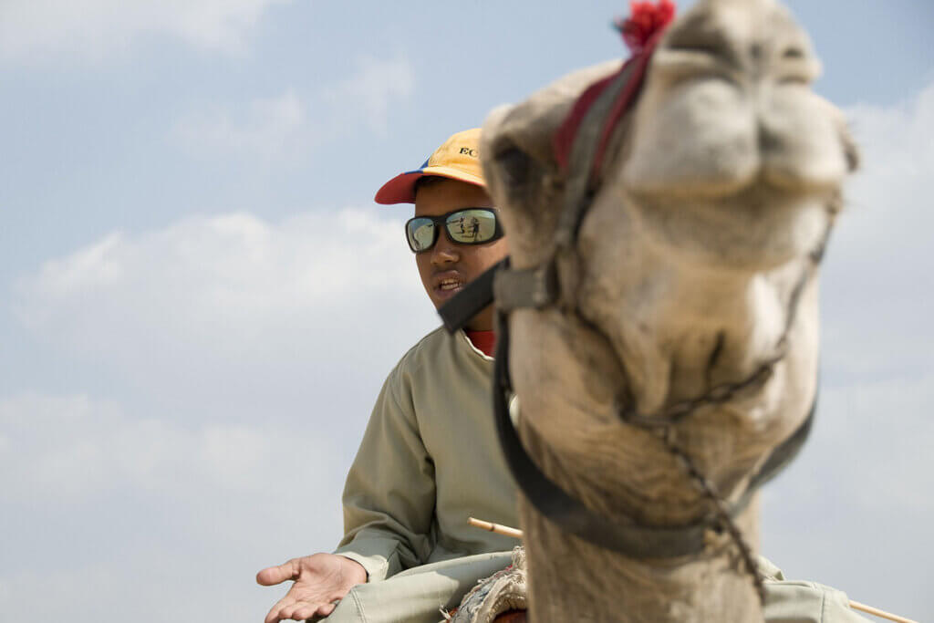 Ein Mann mit Sonnenbrille sitzt auf einem Kamel.