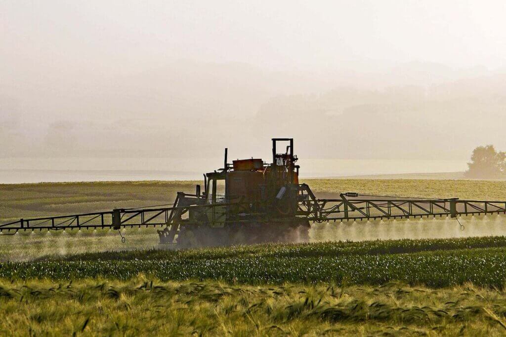 Traktor versprueht Pestizide ueber Acker