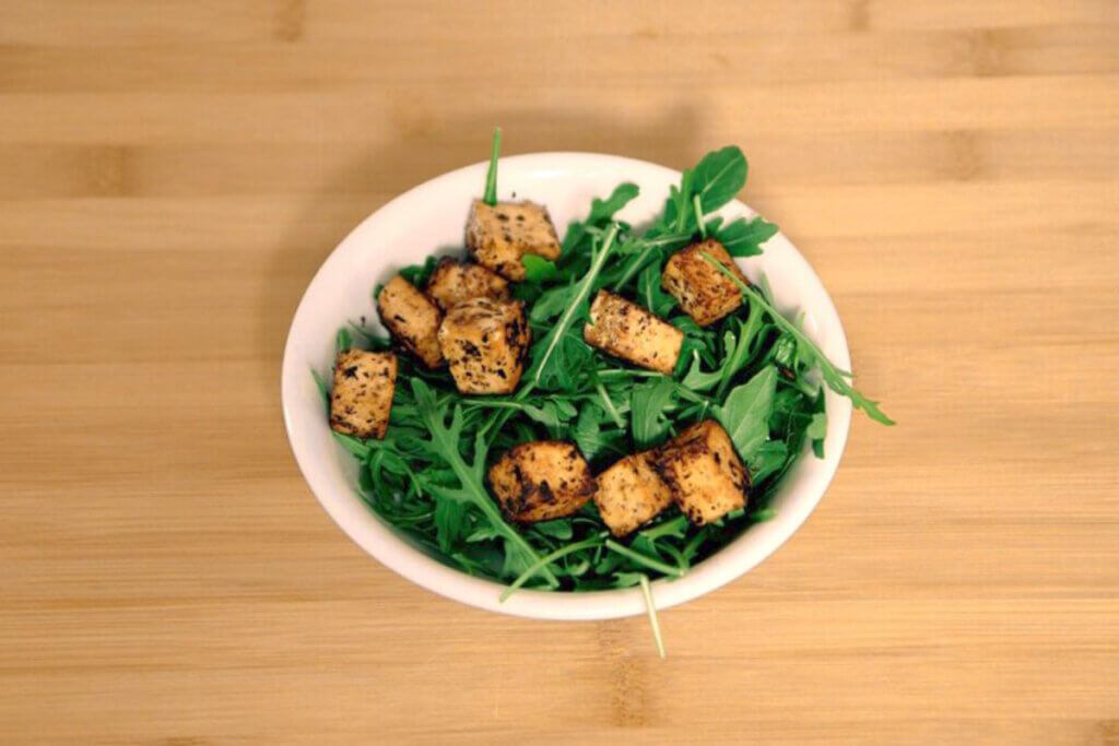 Ein Teller mit Kräutertofu und Salat auf einem Holztisch.