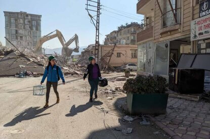 Zwei Frauen laufen durch einen zerstörten Ort.