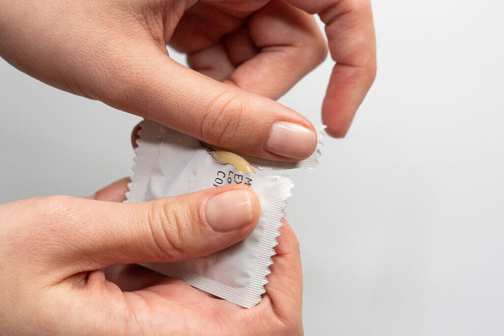 Person reisst Kondomverpackung auf