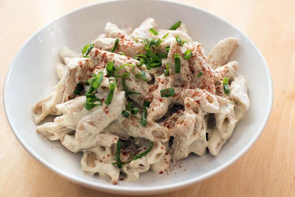 Nudeln mit Cashew-Kease-Sauce, garniert mir gruenen Fruehlingszwiebeln in einem weißen tiefen Teller.
