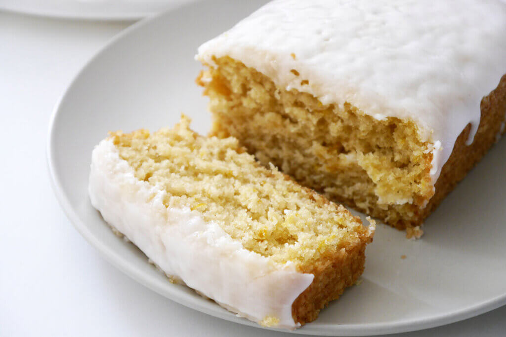 Ein angeschnittener Zitronenkuchen mit Zitronen-Glasur auf einem weißen Teller.