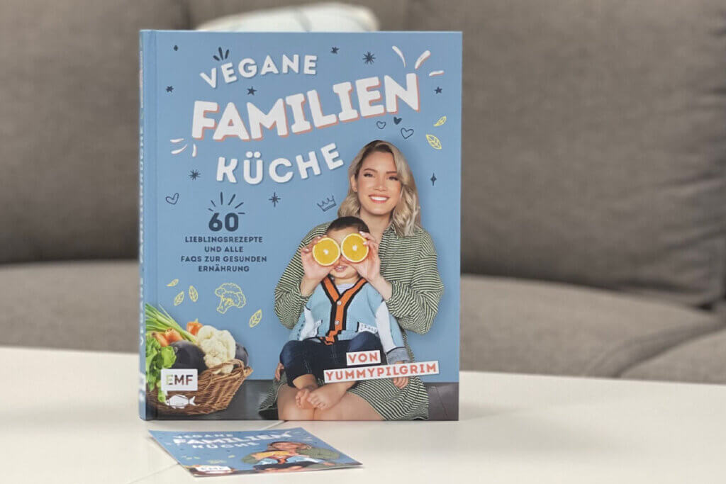 Buchcover Vegane Familien Kueche. Buch steht auf einem weissen Tisch.