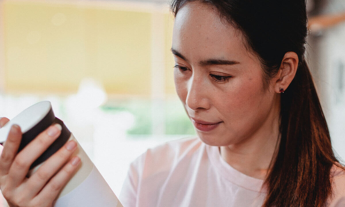 Frau mit schwarzen Haaren in pinkem Shirt liest eine Produktverpackung.
