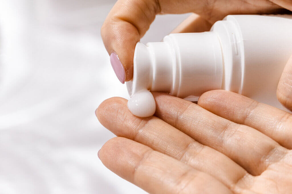 Person pumpt sich aus einer weissen Produktflasche Shampoo auf die Finger.