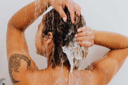 Person shampooniert sich ihr schwarzes Haar unter der laufenden Dusche.