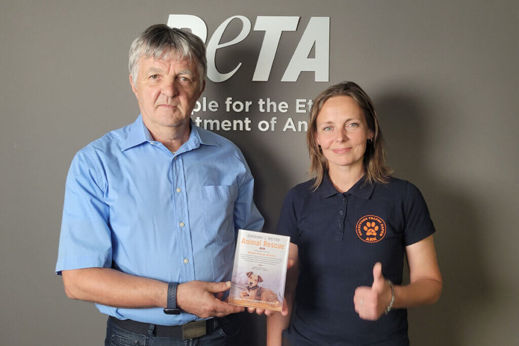 PETA Vorstand Harald Ullmann im blauen Hemd ueberreicht eine Urkunde an eine Frau im schwarzen Shirt von Animal Rescue Kharkiv.