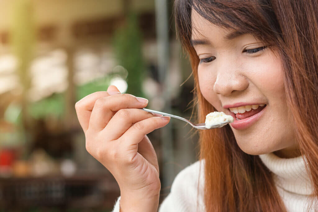 Frau isst mit einem Loeffel Joghurt.