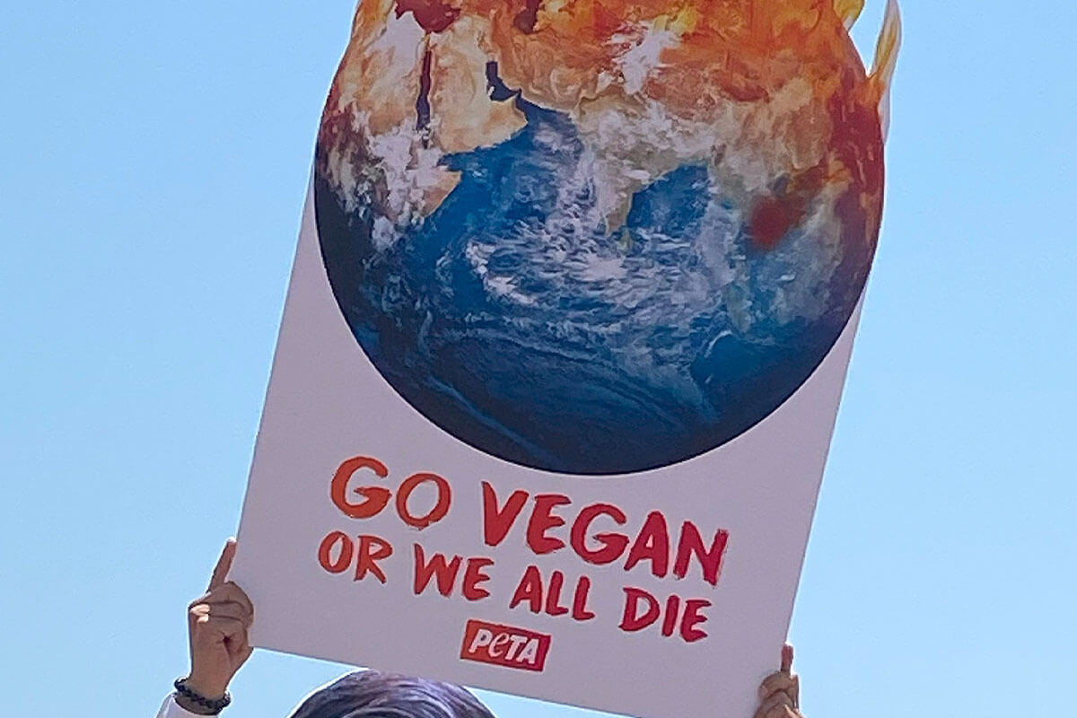 Demonstrant haelt ein Schild mit einer brennenden Erde auf der steht: Go vegan or we all die.