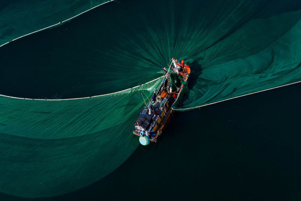 Ein Fischerboot mit weit ausgespanntem Netz im Meer.