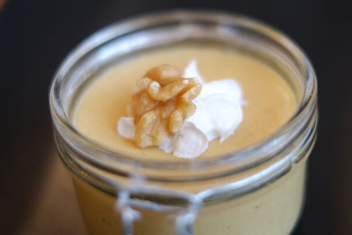 Veganer Kuerbispudding garniert mit Sahne und Walnuss in einem Glas.