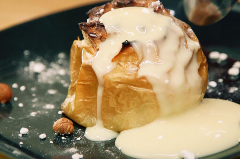 Veganer Bratapfel mit Vanillesauce auf einem dunklen Teller.