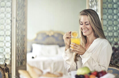 Eine Frau fruehstueckt in einem Hotelzimmer.