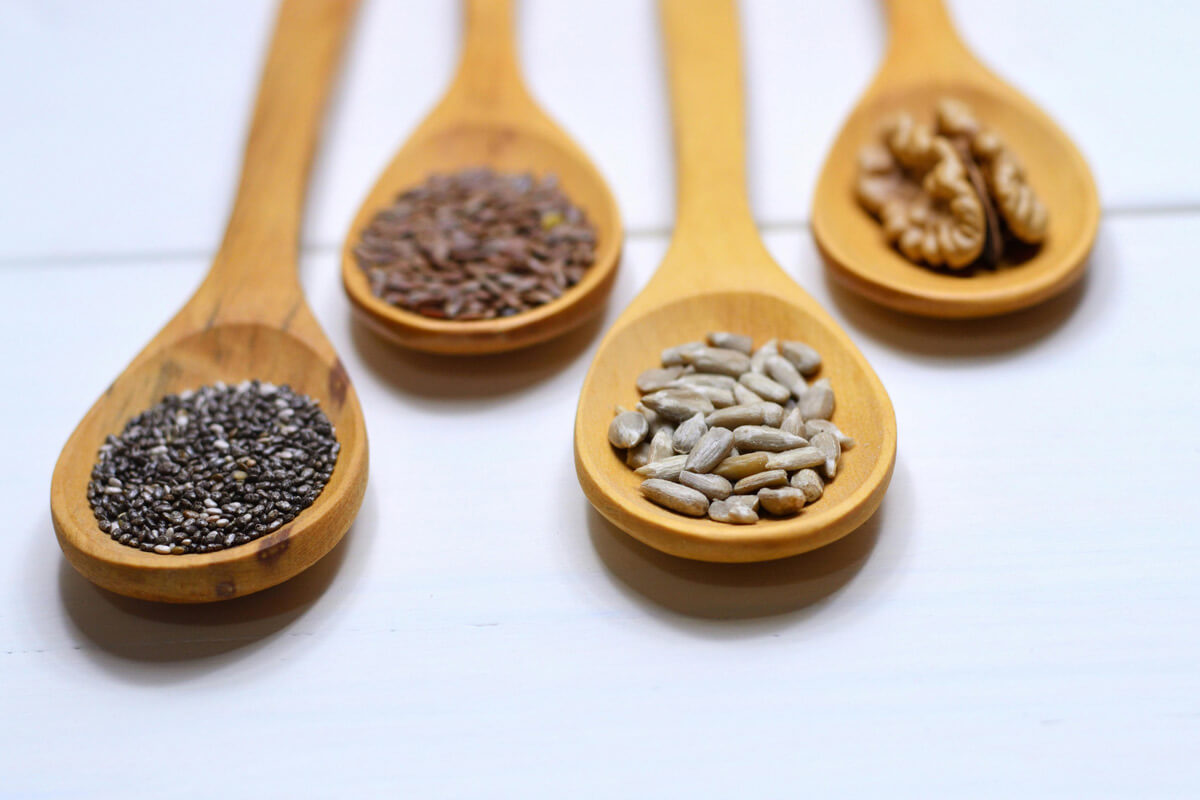 Löffel mit Chiasamen, Leinsamen, Sonnenblumenkernen und Walnüssen als pflanzliche Omega-3-Quellen.