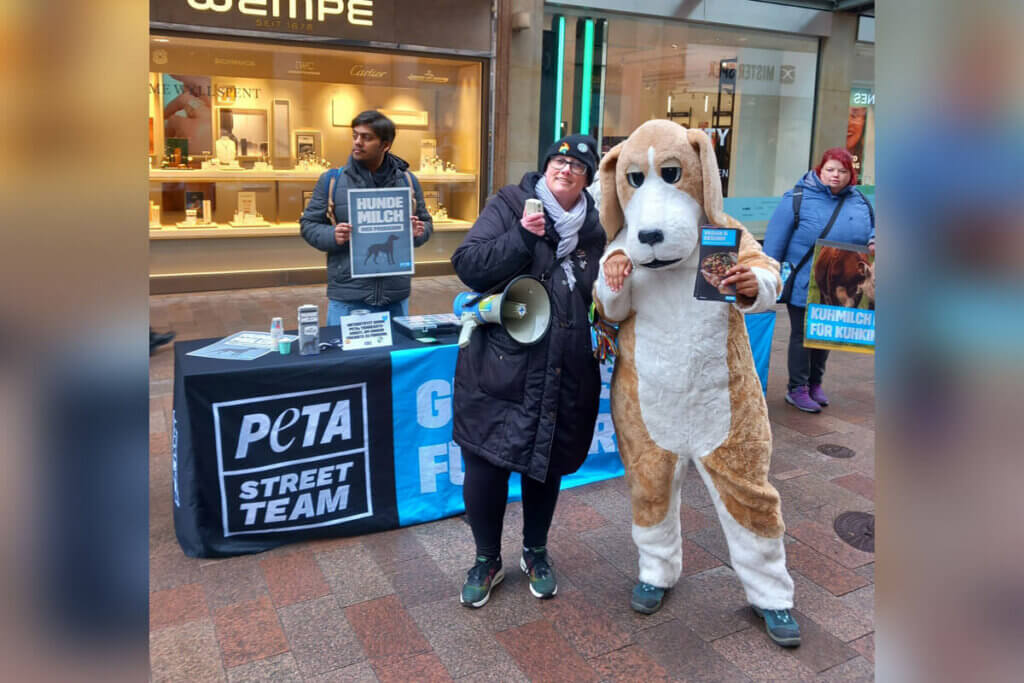 PETA Stand in der Innenstand mit 3 Personen. Eine Person im Hundekostüm.