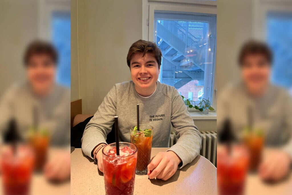 Milan sitzt an einem Küchentisch und trinkt einen Mocktail.