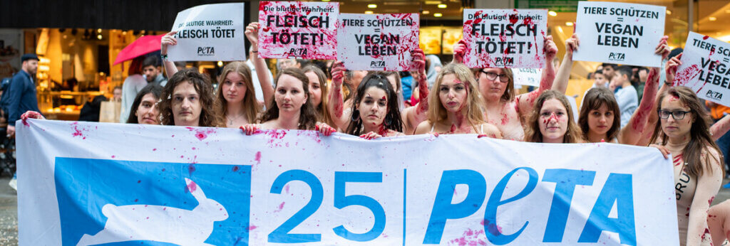 ausgezogene Menschen mit Kunstblut halten einen Banner in der Hand mit der Auffrischt 25 Jahre PETA Deutschland. Sie demonstrieren gegen Fleischkonsum