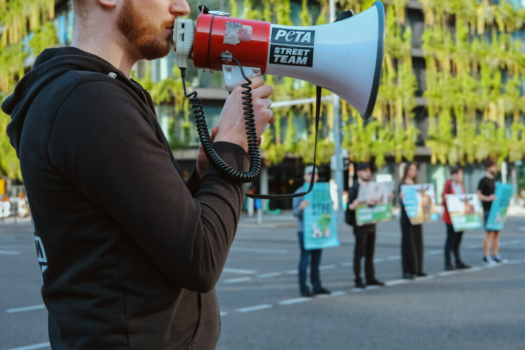 Person mit Megafon und im Hintergrund Menschen mit Demoschildern
