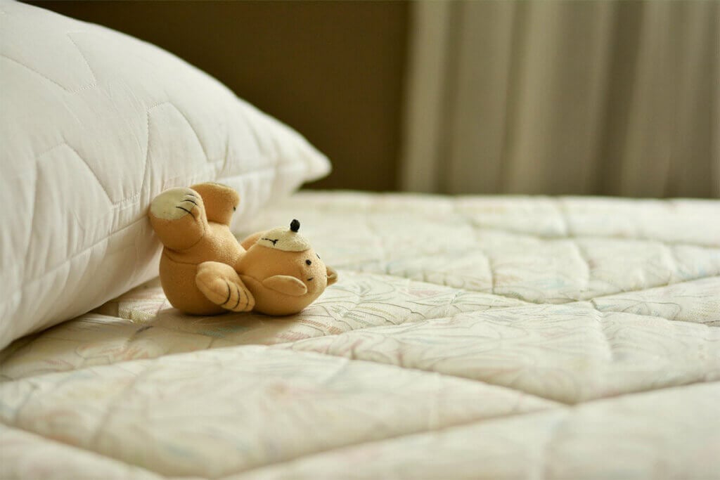 Ein Teddy liegt mit angelehnten Beinen Richtung Kissen.