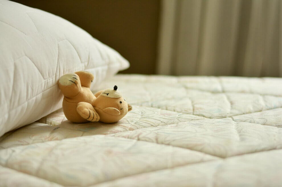 Ein Teddy liegt mit angelehnten Beinen Richtung Kissen.