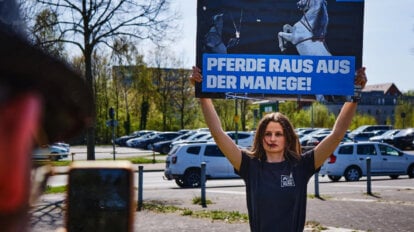 Perosn hebt Schild mit Aufschrift "Tiere raus aus der Manege" hoch und wird fotografiert