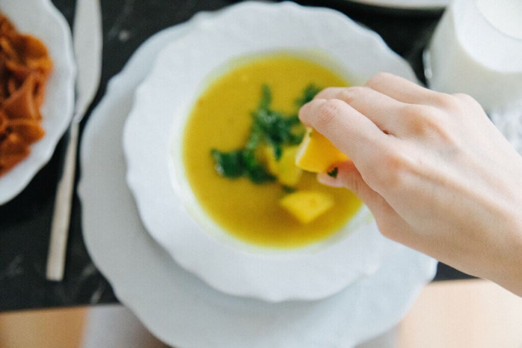 Hand zerquetscht Zitrone über Linsensuppe in Teller